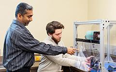 Professor pointing to machine in box.